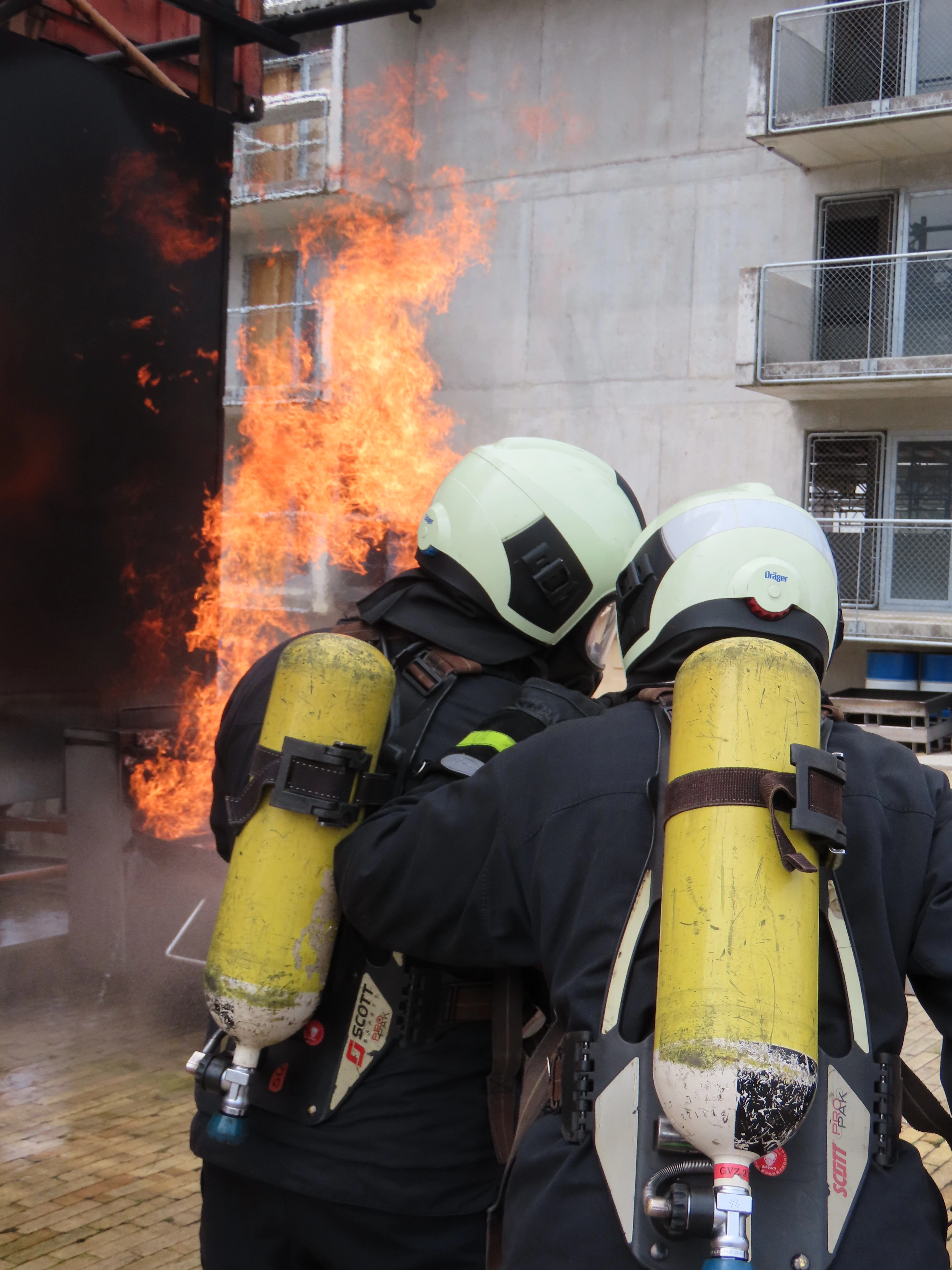 Das Bild zeigt Paul bei der Feuerwehr, wie er vor einem Feuer steht und sich mit einem Kollegen bespricht. Dabei hat er die komplette Schutzausrüstung inklusive Atemschutzgerät an.